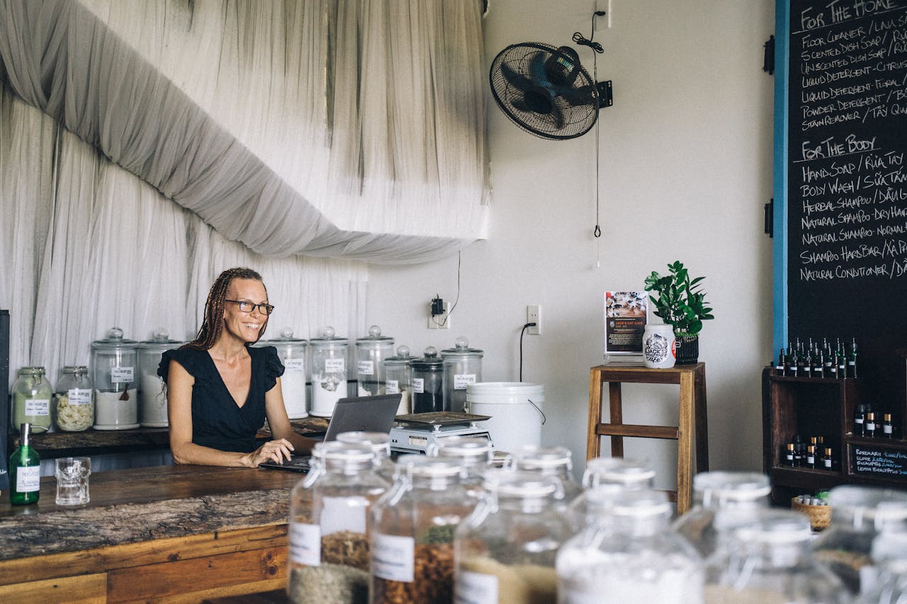Smiling woman working on laptop in organic eco-friendly shop with glass jars.